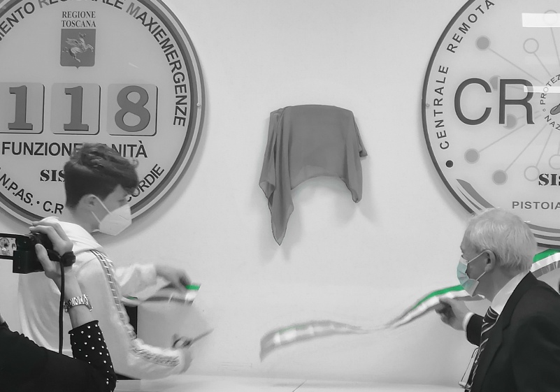 Nella foto, in bianco e nero, il figlio del dottor Nicola Roccella taglia il nastro tricolore. Sulla destra il logo della CROSS, sulla sinistra quello del 118. Insieme al figlio il padre di Nicola 